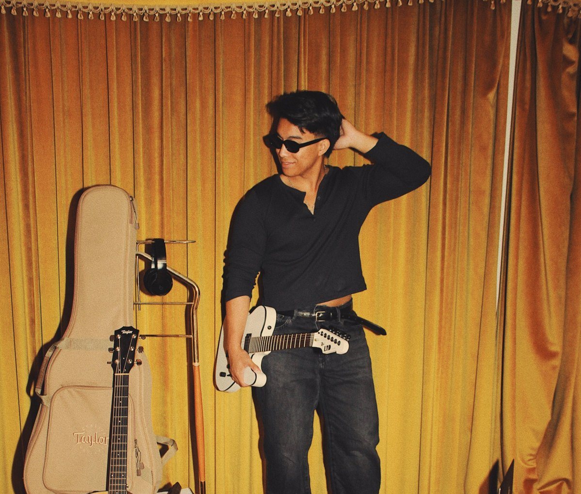 Aut with a white guitar in front of gold velvet curtains